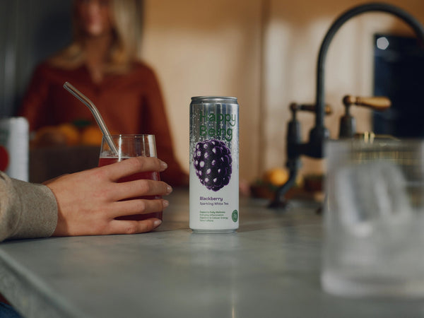 Happy Being Blackberry Sparkling White Tea can beside a glass of iced tea on a kitchen counter.