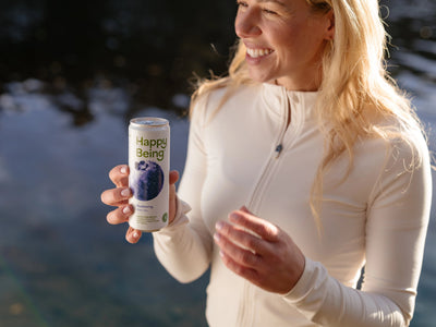 Woman holding Happy Being Blueberry White Tea outdoors in winter sunlight.