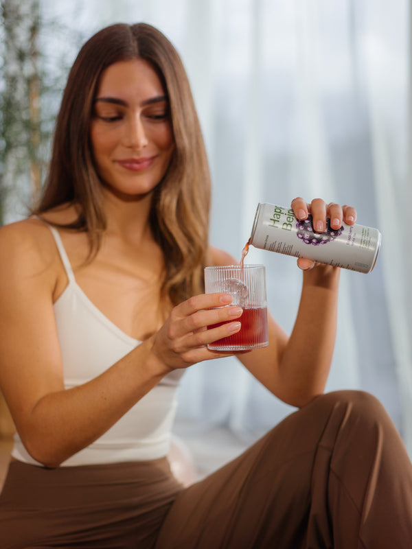 Woman pouring Happy Being Blackberry white tea into a glass, smiling and enjoying the drink.