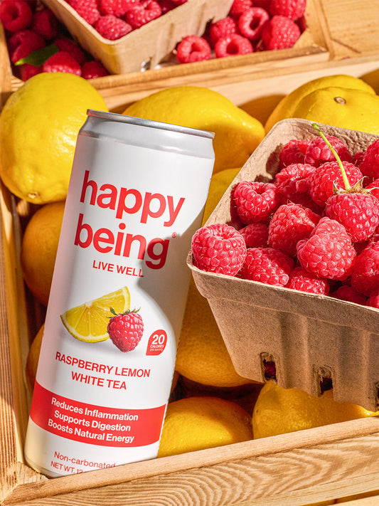 A can of Happy Being Raspberry Lemon White Tea styled among fresh lemons and raspberries on a clean surface.