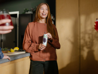 Happy Being wellness drink cans displayed with fresh turmeric, elderberry, and citrus ingredients on a bright kitchen counter.