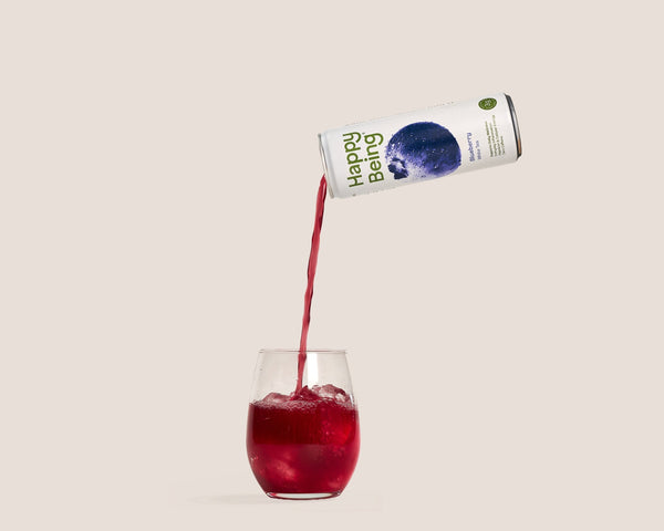 Happy Being wellness drink poured over ice into a glass on a soft neutral background.